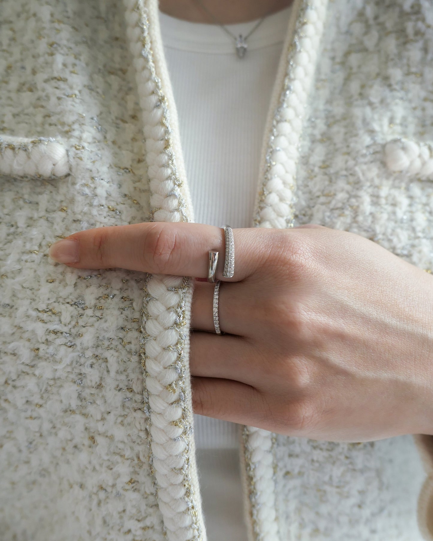 woman neck down in a white and cream tweed jacket, holding the jacket edge with her hands, with two 18k white gold lab grown diamond rings on her fingers