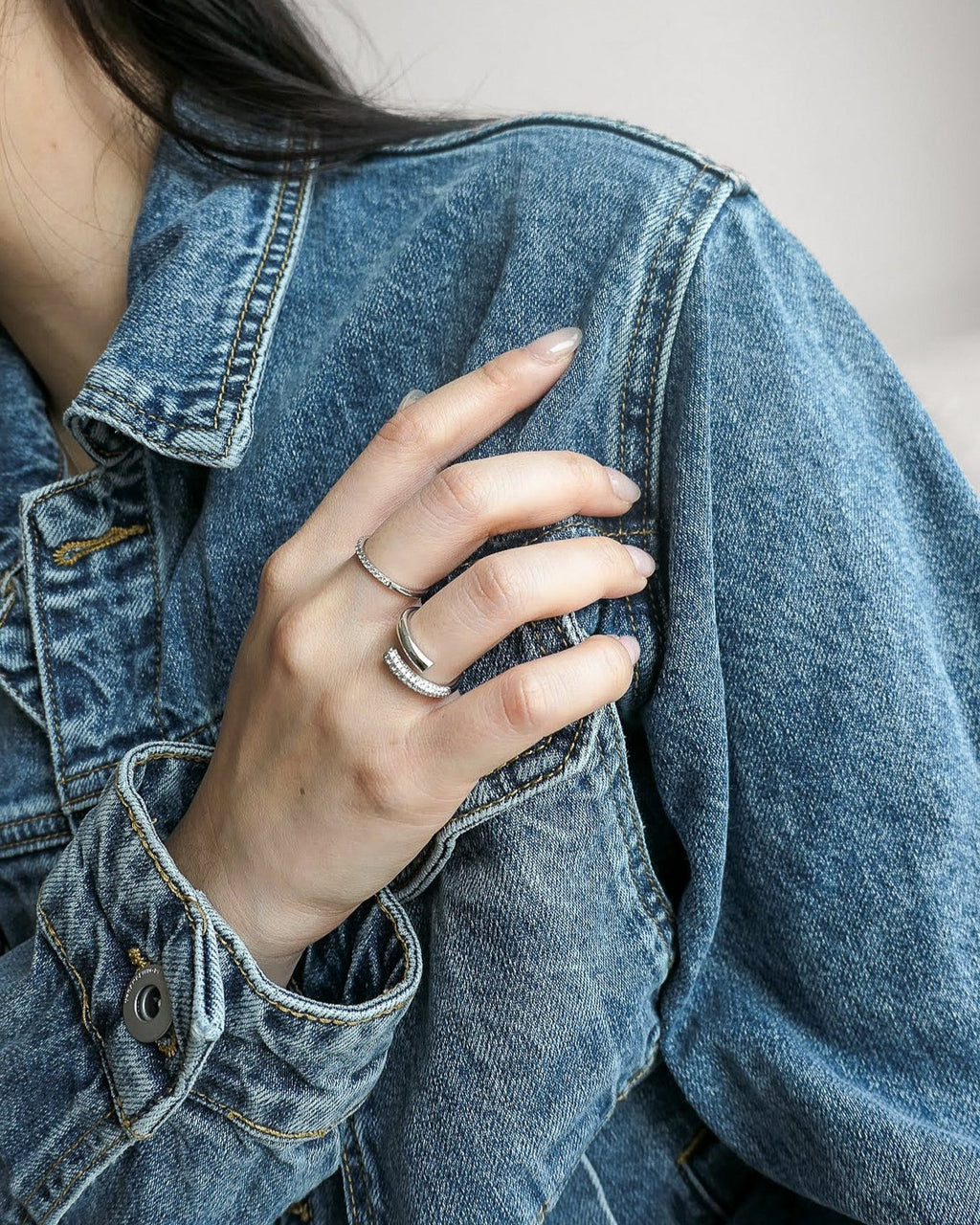 woman neck down in a denim jacket, hand resting across her chest with two 18k white gold lab grown diamond rings on her fingers 