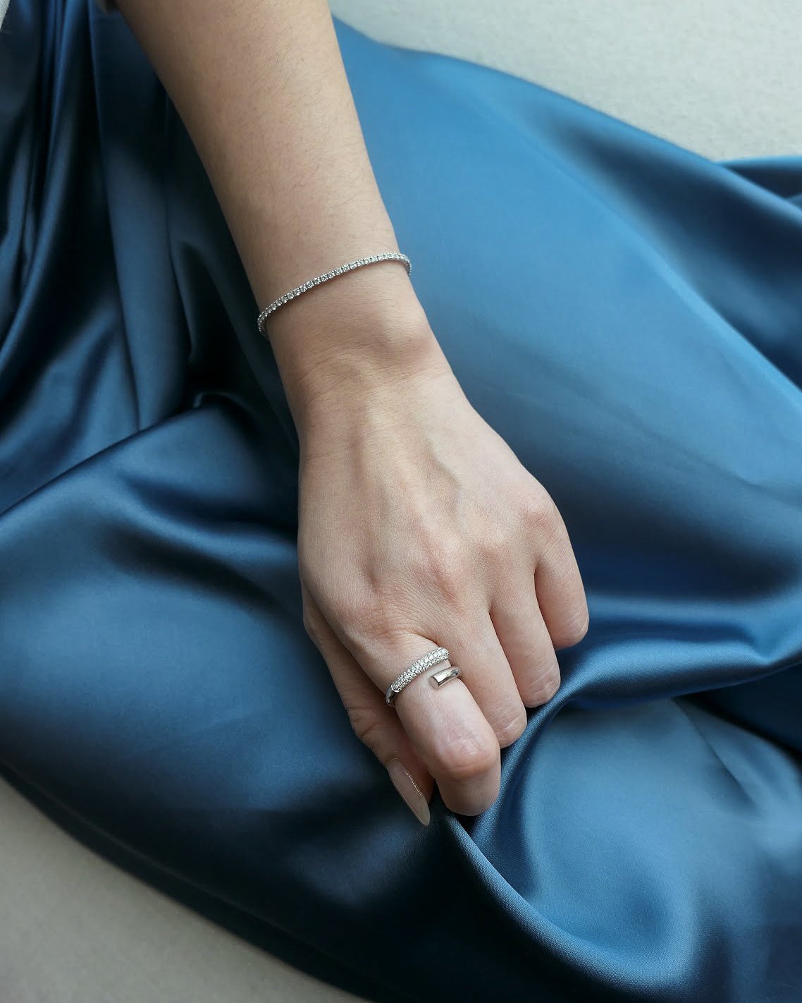 woman sitting down, waist down, wearing a blue silk skirt, hand resting on lap, wearing an 18k white gold diamond tennis bracelet on wrist and diamond ring on finger